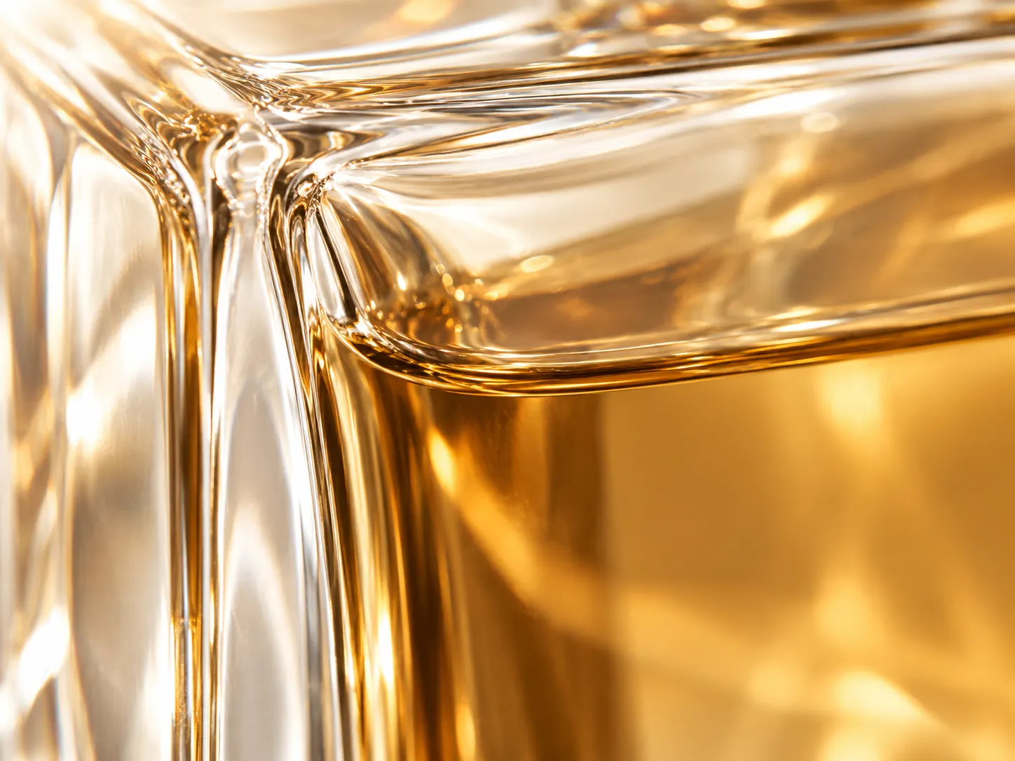 Light refracting through a sculpted glass edge and amber perfume